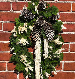 A contemporary holiday wreath uses bold green evergreens like fresh Hinoki cypress and mixes them with dried and bleached oak leaves, hanging amaranthus, and pine cones.