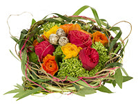A creative nest of barked wire, lily grass, bay leaf, curly willow, collared wire, bullion, and yarn is the perfect setting for an accent of red, yellow, and orange spring flowers.