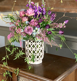 A foam-free vase arrangement in purple and dusty pink hues features magnolia branches, Italian ruscus, tulips, roses, hydrangeas, stock, heather and jasmine vine.