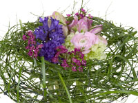 A nest fashioned from deciduous huckleberry with long blades of beargrass wrapped and woven in. In the center is an arrangement of miniature hydrangea, hyacinths, ranunculus, parrot tulip, and wax flowers.