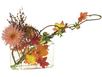Coral dahlia buds and blooms delight in this arrangement, complimented by a burst of grains and several silk autumn leaves in a clear glass container holding an armature fashioned from bare kiwi branches.