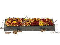 A variety of small chrysanthemum blooms peak out of a low, shallow rectangular container, their shades of yellow, deep red, and bi-color creating depth and texture. River rocks and sweet gum pods lay sparingly in and around the container.