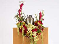 An elegant cascading design for holding a cremation urn combines such floral materials as red roses, light green amaranthus, pale yellow orchids, ginger, and galax leaves.