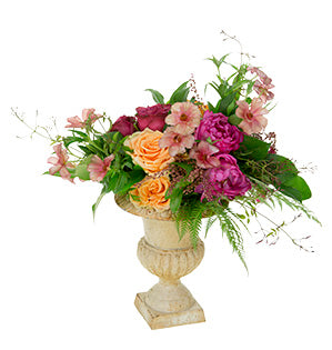A beautiful boho style wedding floral design in a peach and pink color palette combines different kinds of garden roses, hanging amaranthus, and local flowers and foliage in a lovely garden urn.
