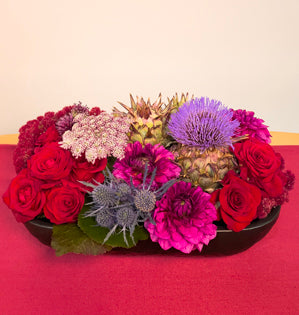 A vibrant textural design full of artichoke, galax leaves, amaranthus, red roses, dahlias, allium, Queen Anne's lace, and eryngium.