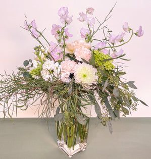A tall bouquet full of movement and soft colors using willow eucalyptus, seeded eucalyptus, garden roses, carnations, chrysanthemum, hydrangea, and sweet peas, woven into a natural armature made from curly willow.