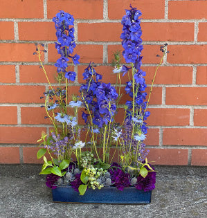 A parallel style floral design mixes flowers in all hues of blue including delphinium, eryngium, nigella, and blueberries.