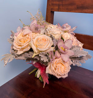 A beautiful bridal bouquet comprised of, Princess Maya garden roses, blush carnations, astilbe, cymbidium orchids, and dusty miller, tied together with a soft pink ribbon.