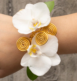 A gold wire wrist cuff is accentuated with two miniature Phalaenopsis white orchids and pieces of spiraled wire.