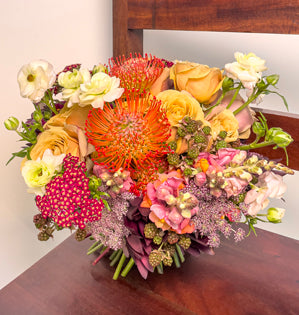 A vibrant wedding bouquet in beautiful fall colors created using golden mustard roses, pin cushion protea, butterfly ranunculus, ornamental blackberries, cottage yarrow, snapdragons, leucadendron, and Queen Anne's Lace.