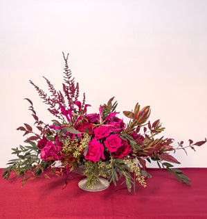A low horizontal arrangement containing, spray roses, garden roses, astilbe, leucadendron, parvifolia, seeded eucalyptus, and nandina, topped with Gloriosa lily.