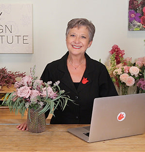 Leanne Kesler, Director of Floral Design Institute stands at her desk with her laptop and a beautiful bouquet placed next to her.