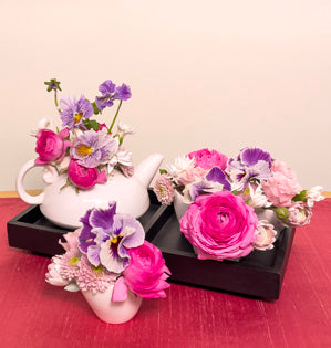 A whimsical spring design made in a tea set using, pansies, ranunculus, spray roses, spray chrysanthemums, star dianthus, and hyacinth.