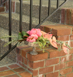 A horizontal arrangement in a shallow elevated compote features anthuriums and peonies in stunning hues of pink and coral.