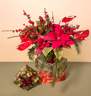 A deep red vase full of lush evergreens, topped with crimson Ilex berries, anthurium, spray roses, and poinsettias.