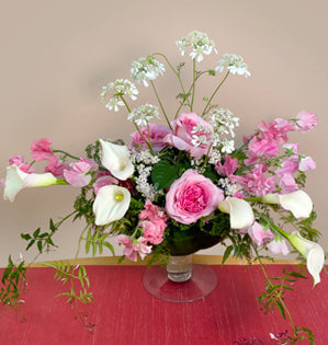 A lovely glass compote design made using, millicent garden roses, orlaya, calla lillies, aspidistra leaves, disflexus, yarrow, jasmine vine, and sweet peas.