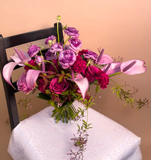 An elegant hand-tied bouquet made with, tulip anthurium, carnations, ranunculus, cool water and blueberry roses, jasmine vine, burning bush, and magnolia leaves.