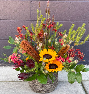 A large woven basket is filled with sunflowers, yarrow, kangaroo paw, grasses, nigella, local foliages, and banksia.