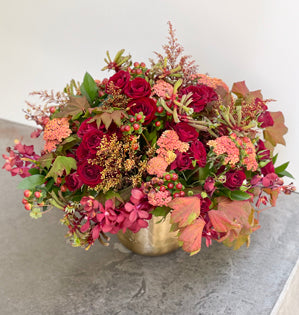 A large foam free design in a brass pot is full of vine maple, Israeli ruscus, spray roses, Mokara orchids, hypericum, dyed solid aster, cottage yarrow and kangaroo paw, all in a beautiful autumn color palette.
