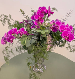 A simple vase design using, deflexus, baptisia, seedum, eucalyptus, and vibrant miniature phalaenopsis orchids.