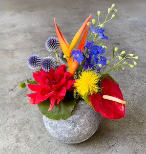 Heliconia, anthurium, dahlia, bella donna, and centaurea in a stone vase.