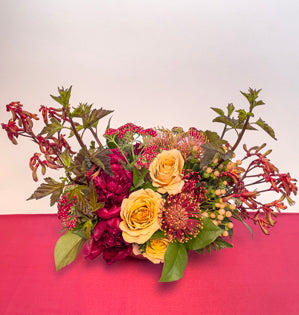 A lovely centerpiece in a sunset palette, using kangaroo paw and peonies, pin cushion protea, golden mustard roses, yarrow, ninebark, hypericum, salal, ruscus and leather fern.