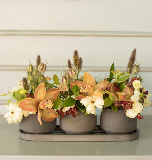 A foam free design mixes a trio of planters full of earthy-hued cymbidium orchids, butterfly ranunculus, kangaroo paw, nigella pods, and blueberries.