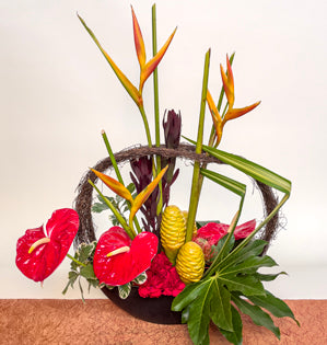 A bold design using topical blooms such as, parakeet heliconia, beehive ginger, and anthurium paired with red carnations, variegated pittosporum, fatsia leaves, leucadendron, leucospermum, and flax stems.