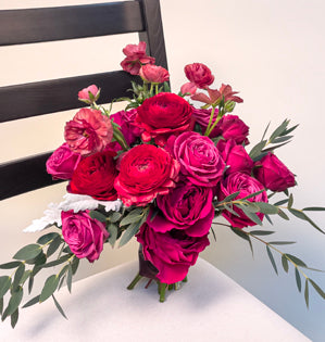 A radiant wedding bouquet full of garden roses, spray roses, ranunculus, butterfly ranunculus, dusty miller, parvifolia, and a single ti leaf, all in tints tones and shades of the 2023 Pantone Color of the Year - Viva Magenta.