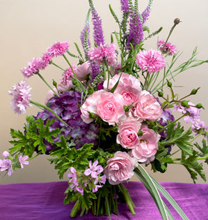 A playful mix of blooms like bachelor buttons, spray roses, and scented geranium.