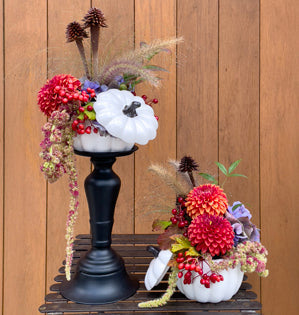 White ceramic pumpkins decorated with orange dalias on black candlesticks.