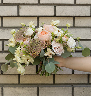 A beautiful romantic hand tied wedding bouquet mixes Juliet roses, butterfly ranunculus, pink lisianthus, carnations, Queen Anne's lace, cottage yarrow, and silver dollar eucalyptus.