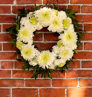 A lush and formal sympathy wreath design features magnum chrysanthemums, carnations, Italian ruscus, plumosa, and aspidistra.