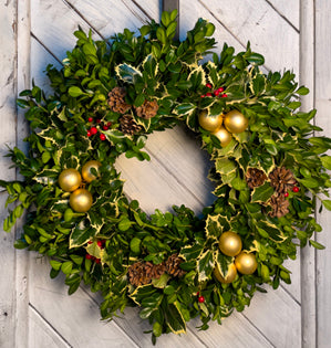 Christmas wreath with gold ornaments and pinecones on a wooden door