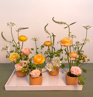 Small centerpieces grouped together containing, peaches n' dream spray roses, ranunculus, orlaya, hypericum, veronica, and bupleurum.
