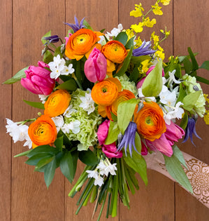 Bouquet of colorful flowers including tulips and ranunculus on a wooden surface