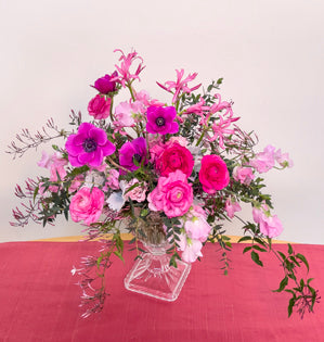 A vibrant and lush compote design in shades of pink made with, dusty miller, parvifolia, jasmine vine, ranunculus, sweet peas, miniature carnations, nerine lilies, and anemones.