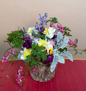 A rustic vase filled with dusty miller, hyacinth, tulips, bluebells, daffodils, and bleeding hearts.