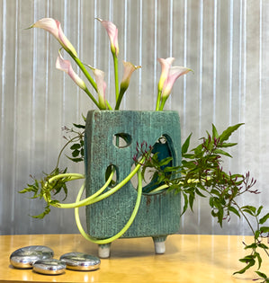 Calla lilies winding through a sculptural vase.