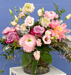 Bouquet of pink and white flowers in a clear vase against a blue background
