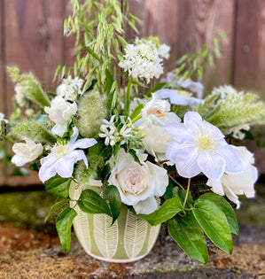 Floral arrangement in a white vase with greenery on a wooden surface