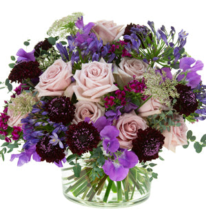 Bouquet of flowers with purple and pink tones in a clear vase on a white background