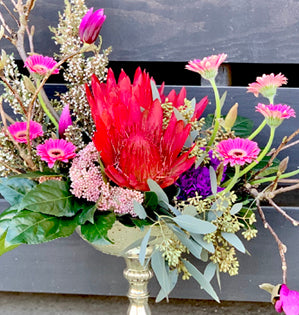 Bouquet of flowers with a prominent red protea in a gold vase.