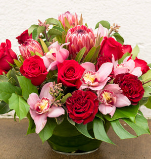 Bouquet of red and pink flowers in a green vase on a neutral background