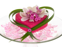 A beautiful Valentine’s Day holiday floral design uses a hot pink heart topped with miniature cymbidium orchids and wrapped in lily grass, all set on a bed of pink sea glass.