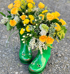 This spring floral design uses children’s green rain boots as a container to hold hyacinth, spray roses, spray mums, hypericum, green trick dianthus, solid aster, pieris, oregonia, and pittosporum for a happy and whimsical effect.