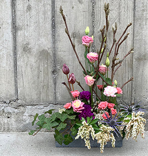 A spring garden arrangement combines budding magnolia branches, foraged ivy, lily of the valley, spray roses, lisianthus, tulips, carnations and eryngium.