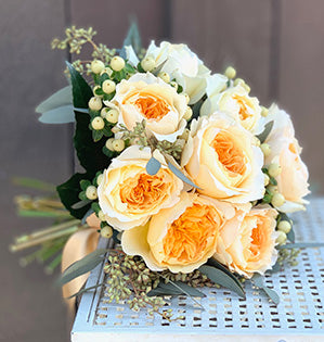 A hand-tied elopement wedding bouquet features Effie garden roses in a beautiful buttery yellow with hypericum, seeded eucalyptus, and fatsia leaves.