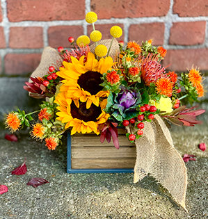 A colorful and rustic garden flower arrangement in yellow and orange color palette features sunflowers, craspedia, and pincushion protea.
