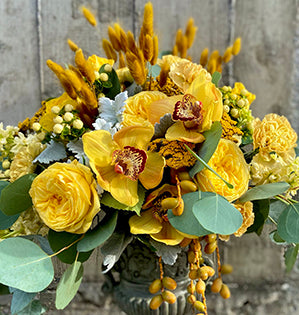 An urn arrangement in the Pantone 2021 Colors of the Year, Ultimate Gray and Illumination Yellow, mixes cymbidiums, carnations, yarrow, stock, dusty miller, and two kinds of garden roses: Catalina and Lemon Pompon.